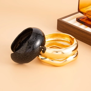 Close-up of golden chunky wavy bangles and black resin bracelet with silver glitter