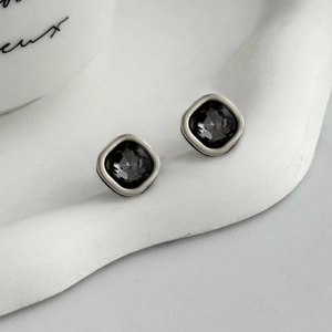 Close-up of geometric square earrings featuring black faceted gems in silver frames