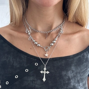 Close-up of layered silver necklaces with cuban chain, T-bar clasp, and cross pendants
