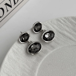 Detail view of oval black faceted gems set in silver metal drop earrings on a white base
