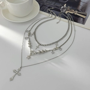 Detail of layered silver necklaces featuring cross pendants and star charms on magazines