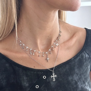 Detail of silver layered necklace with sparkling cross pendant and star charms on a model