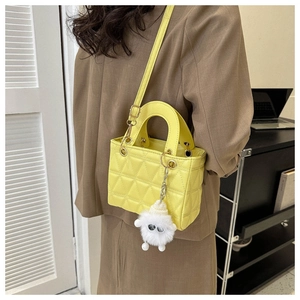 Crossbody wear of yellow quilted mini bag with shoulder strap and plush charm detail
