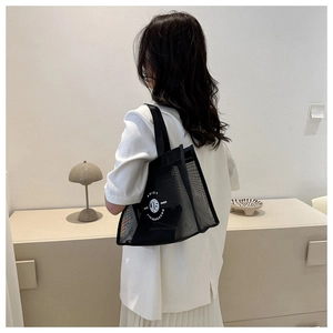 Detailed view of large black mesh tote bag worn over the shoulder with white logo