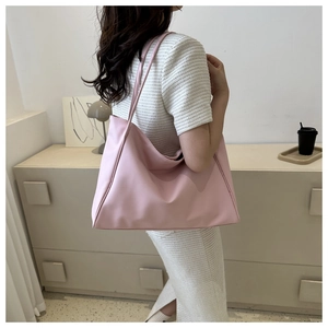 Vue latérale d'un grand sac fourre-tout rose pâle porté à l'épaule dans un décor épuré