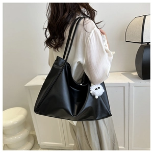 Détail du sac cabas noir minimaliste avec un pendentif en peluche blanc sur la bandoulière