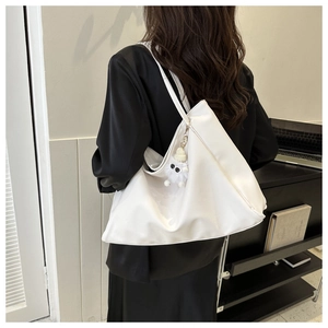 Detail of a large white tote bag featuring a cute plush pendant on a slender strap