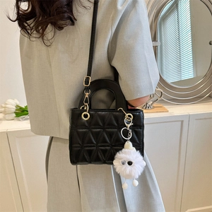 Chic black quilted crossbody bag with circular metal handle and white fur pompom accessory