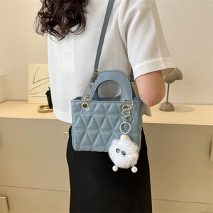 Light blue quilted crossbody bag with plush charm shown on person with hand-held strap