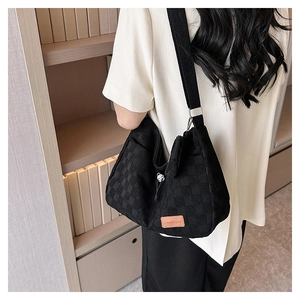 Detail of black checkerboard embossed canvas bag featuring a wide strap and side zip pocket