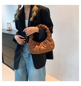 Detail of a brown pleated dumpling handbag styled with a black blazer and casual jeans