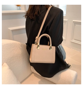 Détail du mini sac beige avec poignée anneau tressée et boucles dorées sur un costume noir