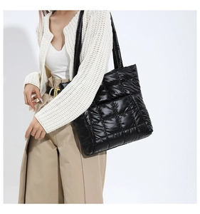 Detailed view of black quilted puffer tote bag in glossy nylon fabric on model