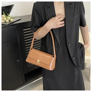 Close-up of a brown retro baguette bag with a golden rectangular clasp on a model