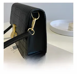 Detalle de herrajes dorados pulidos y textura de cocodrilo en un bolso de hombro negro