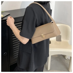 Close-up of beige leather baguette bag with a gold square buckle on a model shoulder