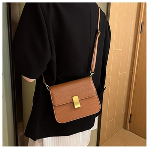 Bolso bandolera marrón con textura de cocodrilo y hebilla dorada mostrado en modelo