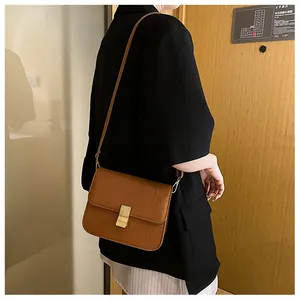 Bolso bandolera marrón con relieve de cocodrilo y cierre dorado sobre traje negro
