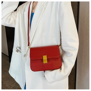 Detalle de bolso bandolera rojo efecto cocodrilo con cierre dorado sobre un traje blanco