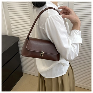 Brown leather baguette bag with gold buckle on model shoulder over white shirt