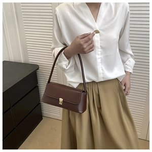 Detail of a vintage dark brown baguette bag with gold buckle worn on a model shoulder