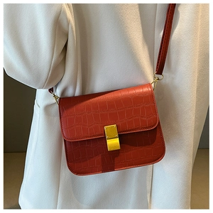 Detalle de bolso bandolera rojo con grabado de cocodrilo y una hebilla dorada fina
