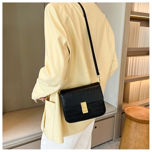Detalle del bolso bandolera negro con relieve de cocodrilo y cierre rectangular dorado