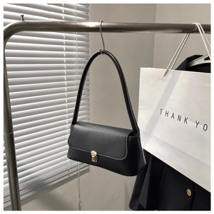 Detail of a black matte baguette shoulder bag with gold metal clasp on a hanger