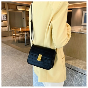 Detalle de bolso bandolera cuadrado negro con patrón de cocodrilo y hebilla dorada