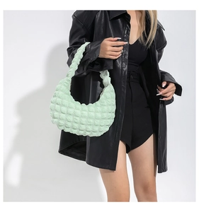 Détail d'un sac demi-lune vert menthe à texture bulles 3D porté sur une veste en cuir noir