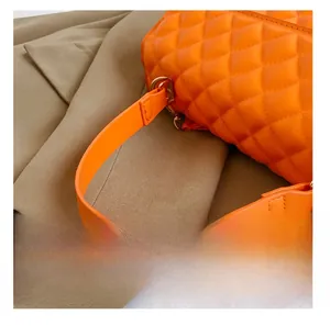 Detail of bright orange quilted handbag showing golden D-ring hardware and stitching
