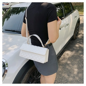Close-up of a white quilted shoulder bag with gold hardware worn by a model in daylight