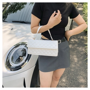 Detail of white quilted crossbody bag with top handle shown in a street style setting
