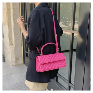 Detail of rose red quilted crossbody bag with golden hardware and top handle strap