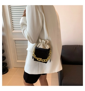 Detail of black crocodile texture bucket bag with gold chain and white drawstring liner