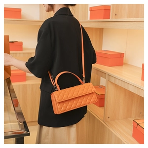 Detail of bright orange quilted leather bag with top handle on minimalist shelf