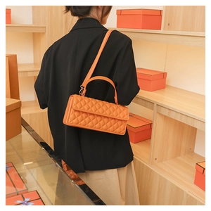 Detail showing the orange quilted leather crossbody bag with top handle worn by a model