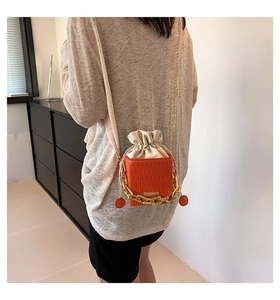 Detailed view of an orange bucket bag with white drawstring and gold chain handle