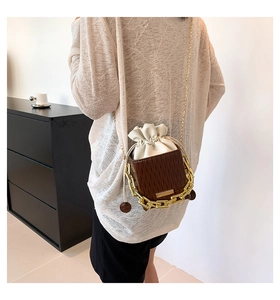 Detail of drawstring bucket bag featuring pleated leather and gold chain strap in a lifestyle set
