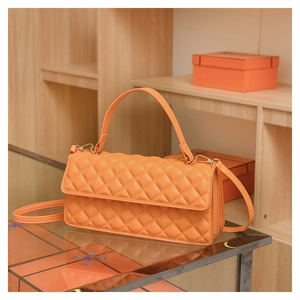 Detail of orange quilted leather handbag with gold hardware on glass surface
