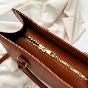 Close-up of smooth golden metal zipper and Saffiano leather texture on a brown tote bag