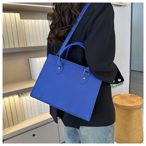 Side view of a bright blue leather tote bag styled with a professional black blazer