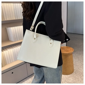 Detail of a minimalist white tote bag with gold rivets and leather handles worn by a model