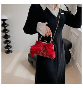 Sac à main en tweed rouge avec chaîne dorée et grand nœud en satin porté par un mannequin