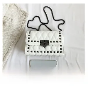 Detail of white quilted crossbody bag featuring black studs and metallic chain strap
