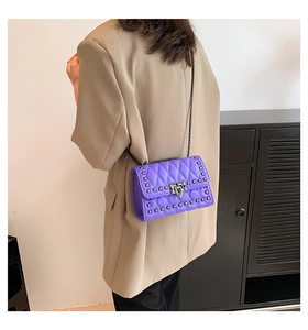 Detail view of purple quilted crossbody bag with metal studs and chain strap on model