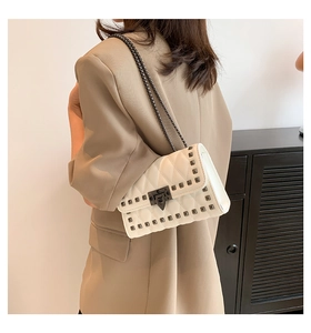 Close-up of a white quilted crossbody bag with dark grey rivets and a metal chain strap