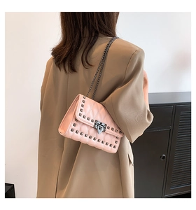 Light pink quilted shoulder bag with dark metal rivets worn by a model in a beige blazer