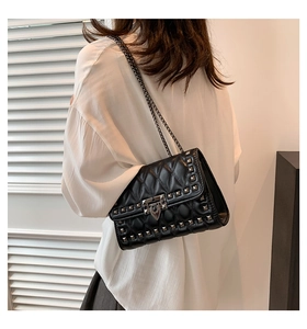 Close-up of black quilted leather crossbody bag with metal rivets and chain strap on model