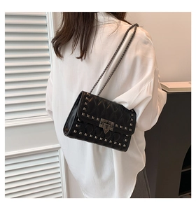 Close-up of black quilted shoulder bag with silver studs and metal chain strap